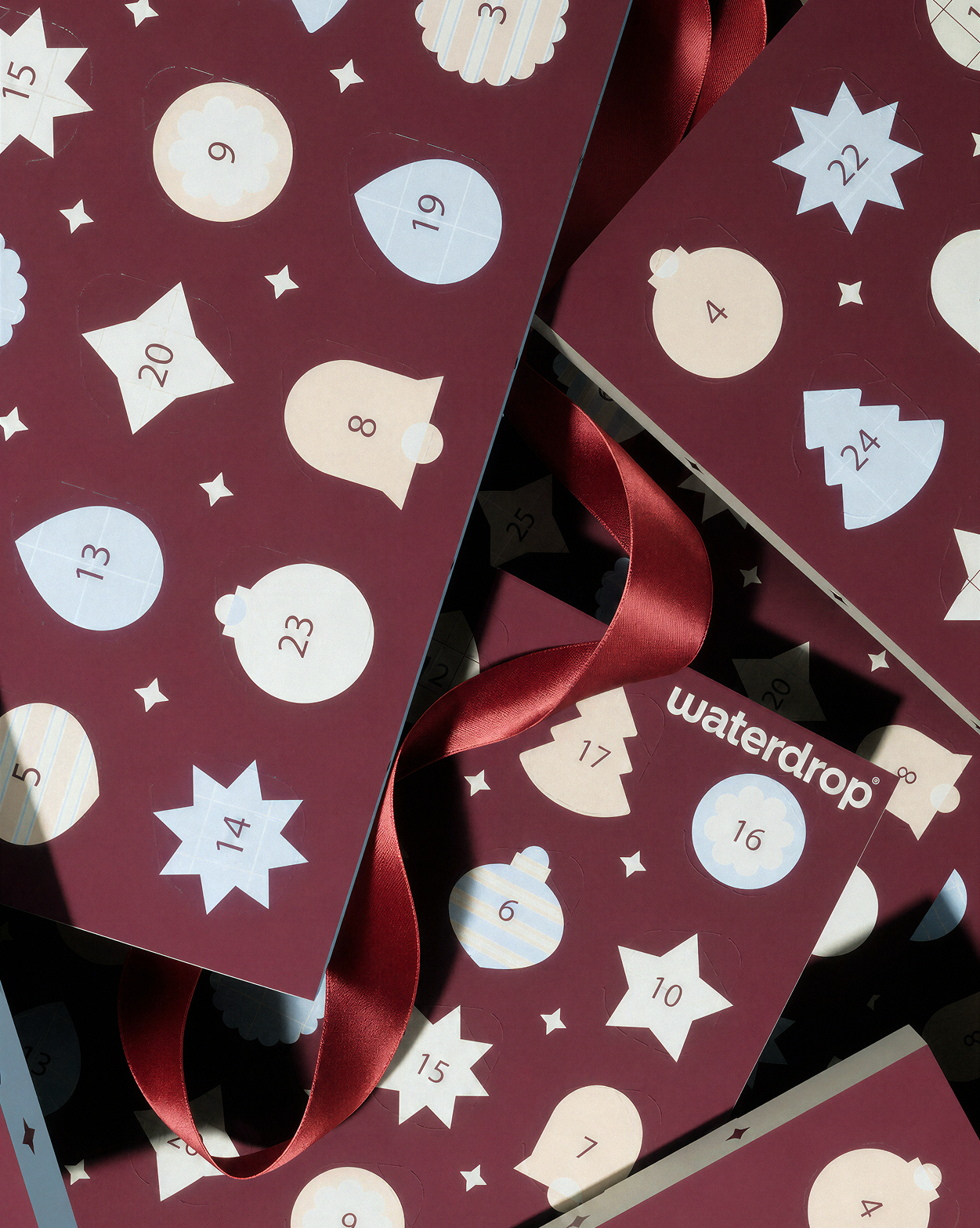 Adventskalender mit nummerierten Türen auf burgunderfarbenen Paneelen und roten Bändern.