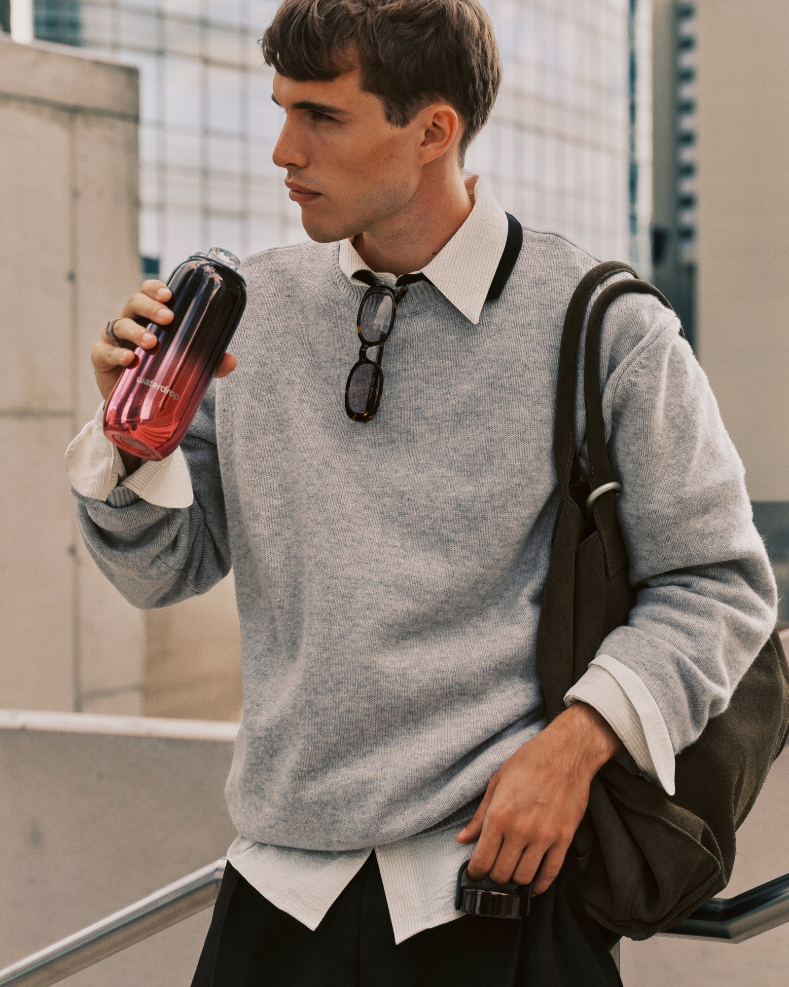 Mann in grauem Sweatshirt und weißem Hemd mit Rucksack trinkt aus einem Becher mit Farbverlauf.