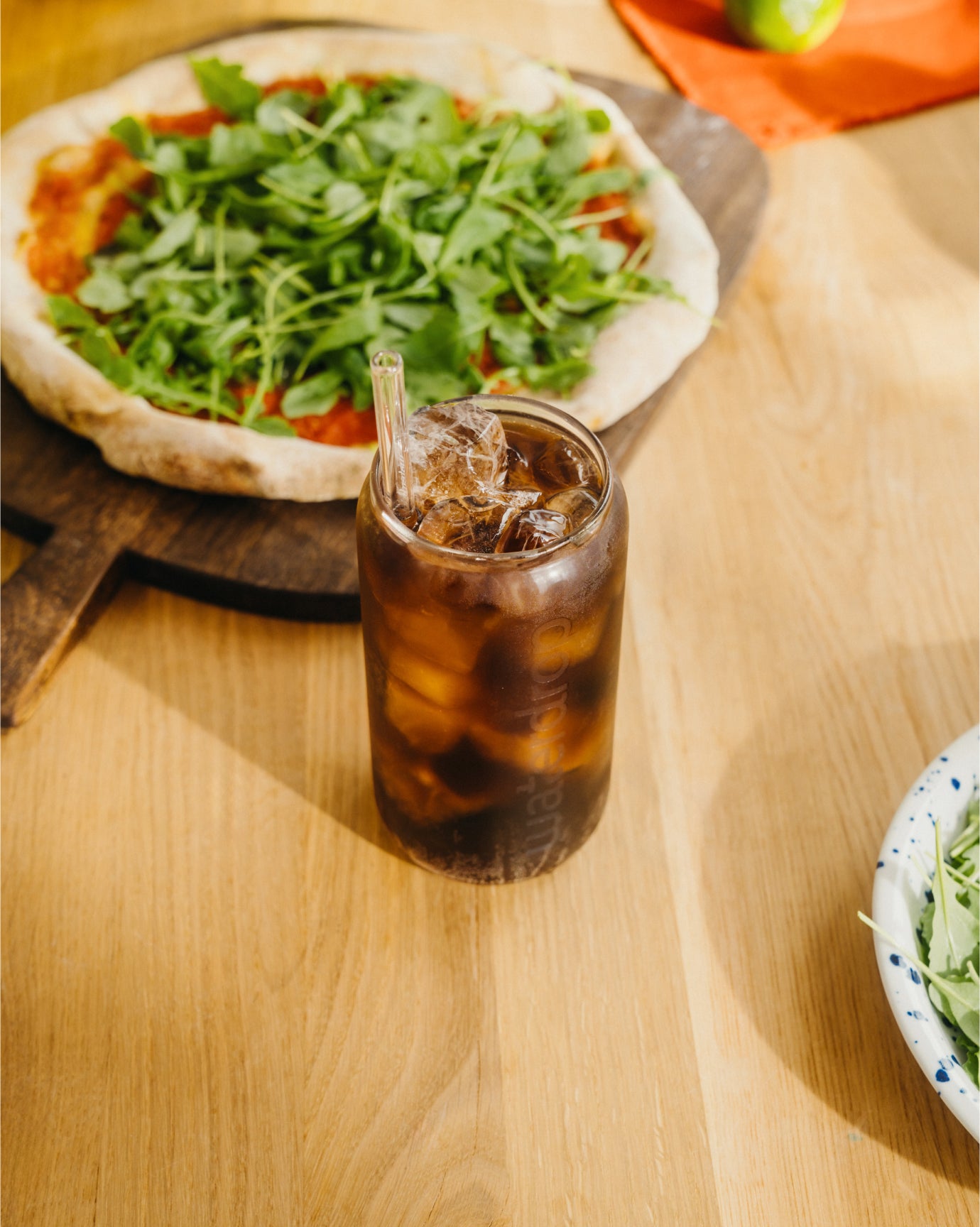 COLA Glass Can mit dunklem Getränk und einer Holzofenpizza.